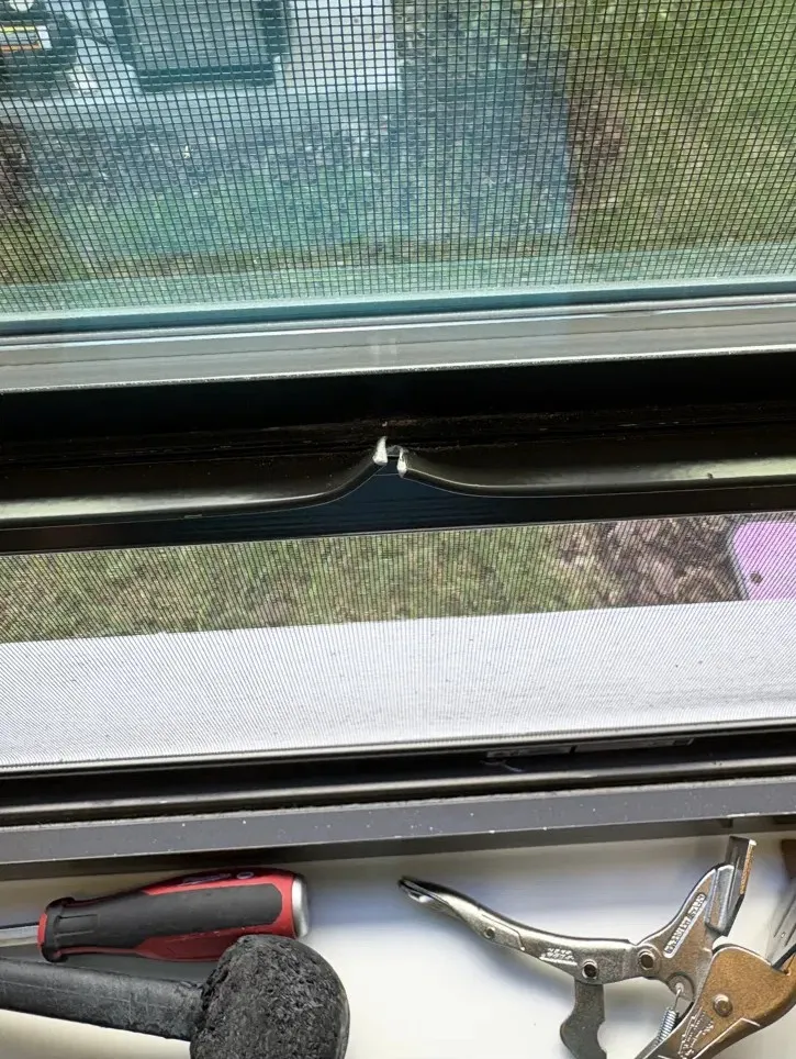 Bent, split bronze window track with repair tools on the sill